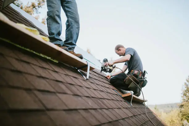 Roofer sealing flashing and replacing damaged shingles on an older El Reno home