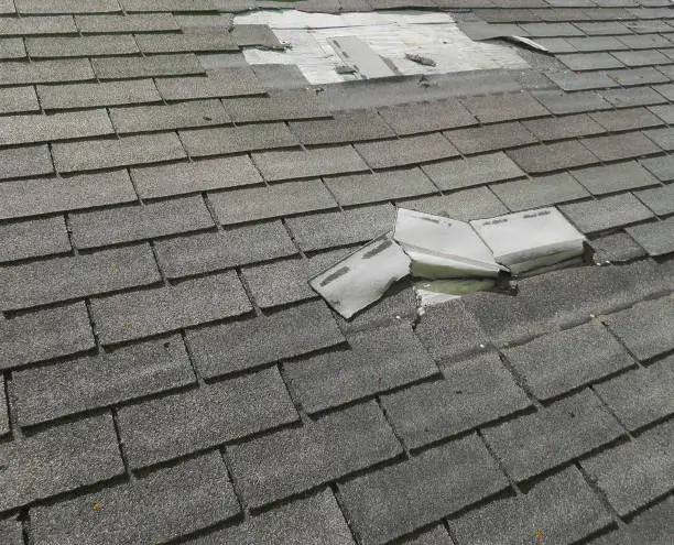 Roofing specialist examining worn shingles and flashing on a storm-exposed home