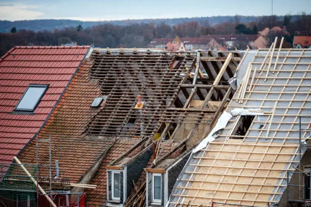 Experienced roofer inspecting roof decking and flashing before full replacement work